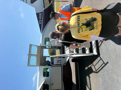       Travelers queue up the steps to board a small tropical propeller plane under a bright blue sky.
  