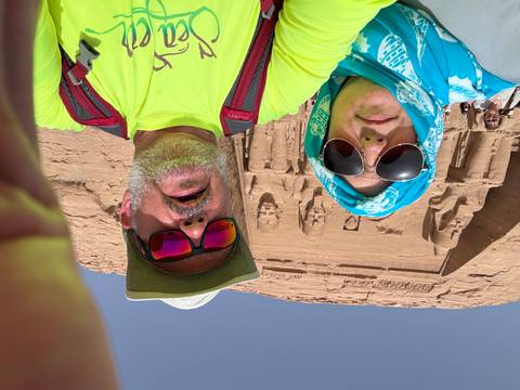       Selfie of two travelers in front of the colossal seated statues at Abu Simbel temple.
  