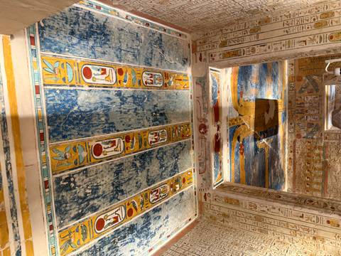       Brilliantly painted blue and yellow hieroglyphic ceiling and walls inside an ancient Egyptian tomb.
  