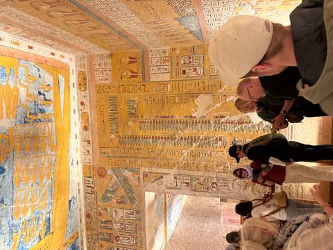       Visitors examine vividly detailed hieroglyphic walls inside an ancient temple chamber.
  