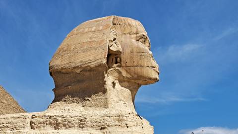       Clear side view of the Great Sphinx’s weathered face against a deep blue Egyptian sky.
  