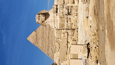       The Sphinx sits before a pyramid with clear delineation under bright sunlight in Giza.
  