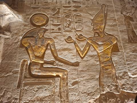       Close-up of golden relief depicting two ancient Egyptian deities exchanging offerings.
  
