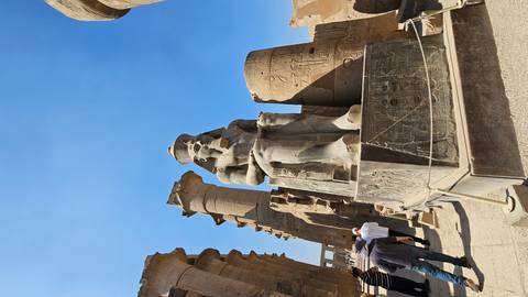       Massive seated pharaoh statue and papyrus-shaped columns inside Luxor Temple courtyard.
  