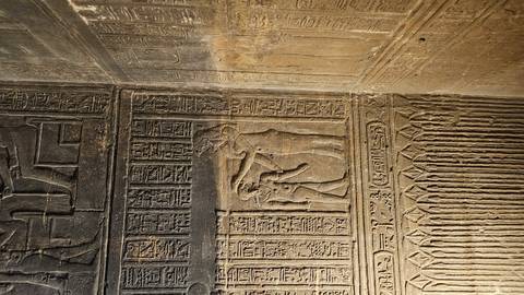       Carved stone reliefs with hieroglyphic columns inside a temple nook lit by warm light.
  