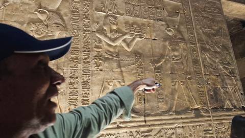       Close-up of a guide pointing out detailed hieroglyphs carved into a sandstone wall.
  