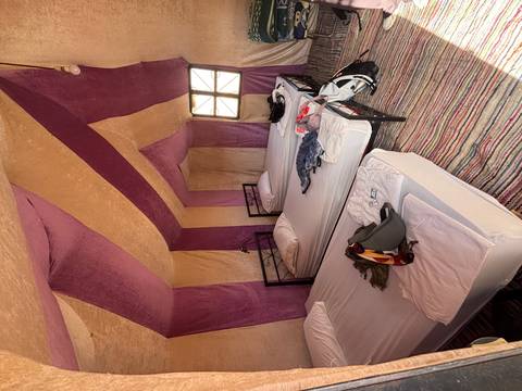       Interior of a desert camp tent with three single beds, colorful textiles and personal luggage.
  