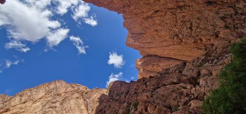       Steep red rock canyon walls and blue sky viewed from the gorge floor.
  