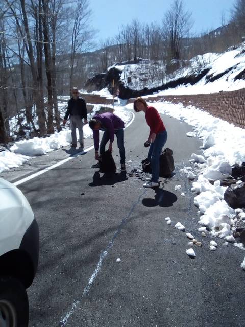       Travellers clear fallen rocks from a snow-lined mountain road on a sunny winter day.
  