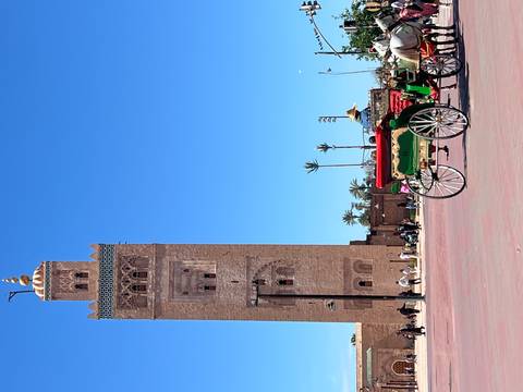       Tall minaret of famous mosque rising against clear blue sky with colorful horse carriage in foreground
  