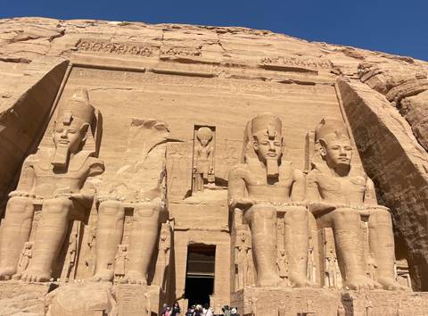       Grand façade of Abu Simbel with four colossal statues carved into sandstone cliff under bright sky.
  