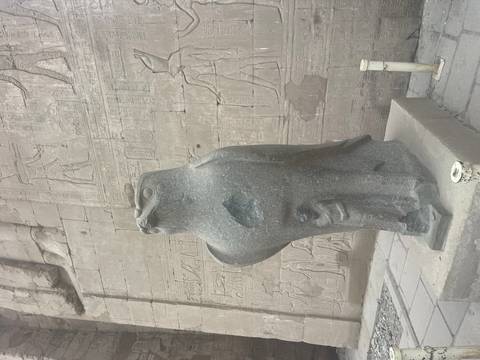       Granite falcon statue of Horus stands before hieroglyph-covered temple wall in Edfu.
  