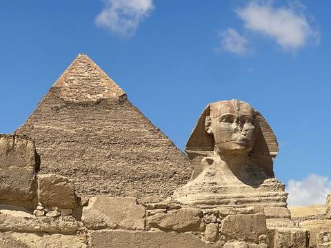       Iconic Great Sphinx with pyramid of Khafre rising behind under clear blue sky.
  