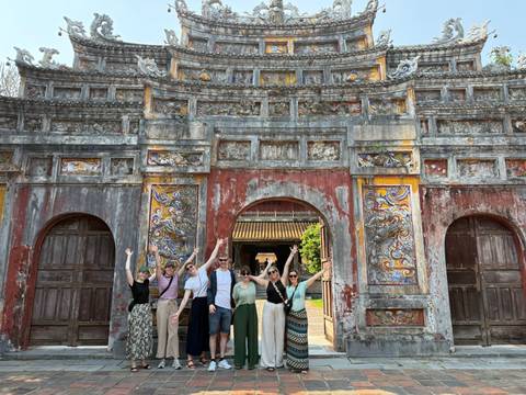       Travel group raises arms in celebration before an ornately carved gate at Hue’s Imperial City.
  