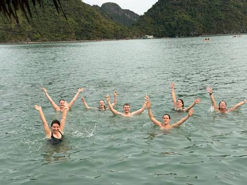       Seven friends splash and cheer while swimming in Halong Bay’s calm green water.
  