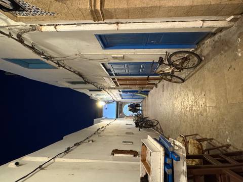      Narrow Moroccan alley at night with blue doors, bicycles and pedestrians under warm lamp light
  