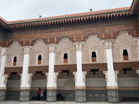       Intricately carved facade and windows of a Moroccan madrasa with visitors admiring the design
  