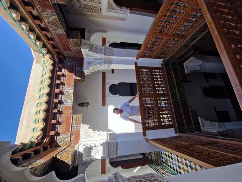       Traveller standing on ornate wooden balcony inside traditional riad courtyard
  