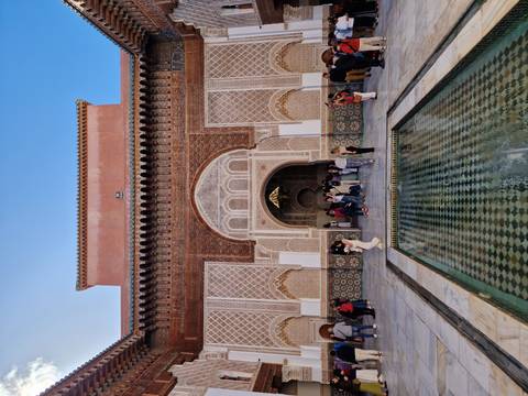       Ben Youssef Madrasa courtyard with reflecting pool and visitors admiring ornate entrance
  