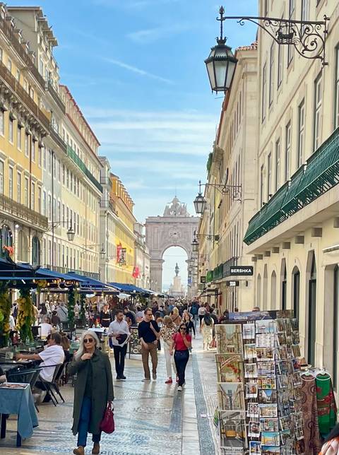       Bustling Rua Augusta in Lisbon lined with colourful façades, café umbrellas and the iconic Arco da Rua Augusta at the end.
  