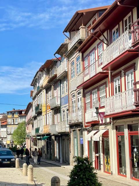       Row of narrow, colourful historic townhouses under blue skies in Porto.
  