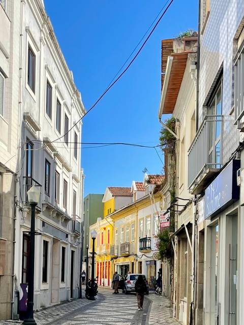       Simple Portuguese street scene with power lines and bright façades beneath a blue sky.
  