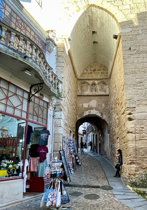       Narrow stone passageway beneath medieval arches with old shopfronts in Tomar.
  