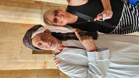       A smiling visitor poses with a friendly local man in traditional headscarf inside an ancient sandstone temple.
  