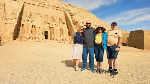       Four travellers stand before the colossal carved façade of Abu Simbel under a vibrant blue sky.
  