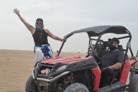       Two adventurers with scarves drive a red dune buggy across a flat desert landscape.
  