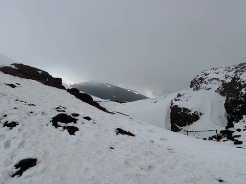       Snow-covered volcanic slopes and dark lava rocks rise into misty clouds on a wintry mountainside.
  