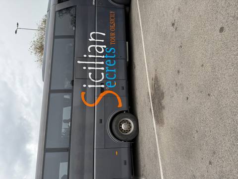       Grey tour bus with large orange and blue 'Sicilian Secrets' branding parked on asphalt.
  