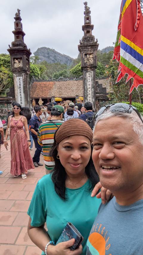       Selfie of a couple at the entrance of an ancient Vietnamese temple crowded with visitors.
  