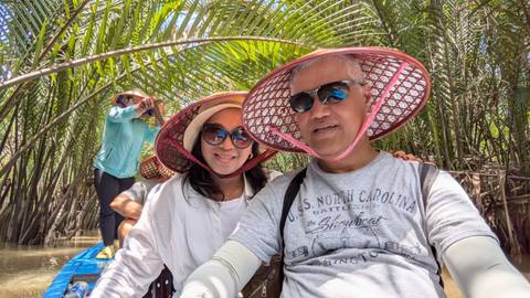       Couple wearing traditional conical hats while boating through dense palm canals.
  