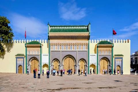       Ornate golden gates of the Royal Palace in Fes with visitors gathered outside
  
