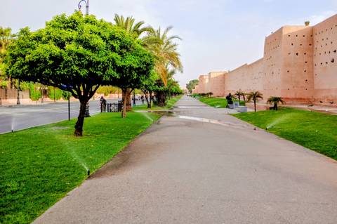       Long walkway beside Marrakech city walls with green lawns and sprinklers operating
  