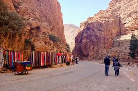      Market scarves hang along road through dramatic red rock walls of Todra Gorge
  