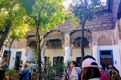       Courtyard of ornate Moroccan madrasa with intricate stucco and zellij crowded by tourists
  