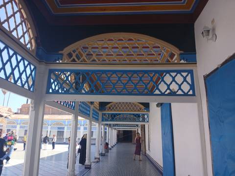       Visitors walk through colorful arched colonnade with geometric latticework in Marrakech palace
  