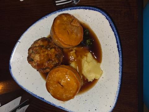       Plate of savory pies with mashed potatoes and gravy in a pub setting.
  