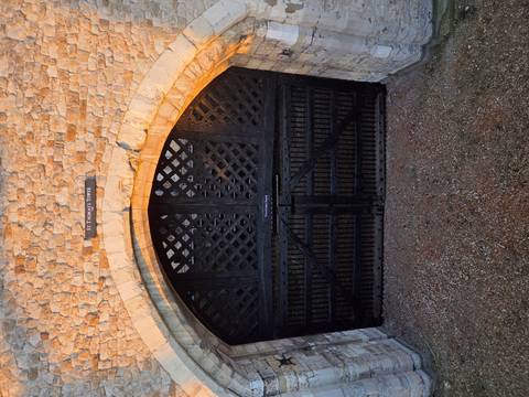       A large black timber gate set within an arched stone wall, marked by a small sign reading "St Thomas's Tower" in warm sunlight.
  