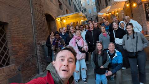       Casual selfie of a tour group on narrow brick steps lined with cafés and warm evening lights.
  