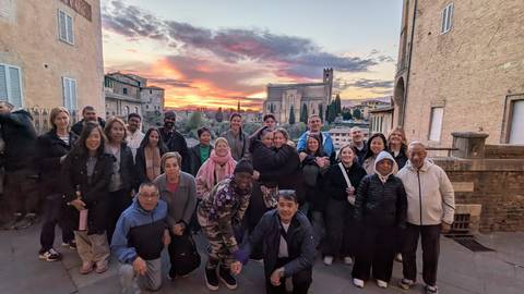       Tour group framed by a colourful sunset over an Italian hill town with church silhouette in the background.
  