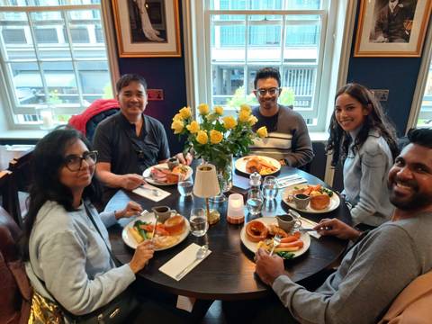       Five travellers share a meal with roast dinners and flowers at a cosy restaurant table.
  