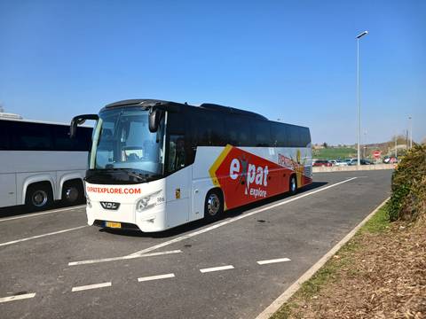       A branded Expat Explore tour coach parked at a service area under clear blue sky.
  