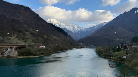      Serene turquoise river winding through a steep mountain valley with snowy peaks under scattered clouds.
  