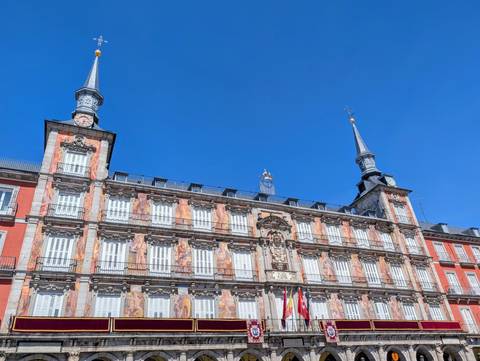       Ornate façade of the Casa de la Panadería on Madrid’s Plaza Mayor glowing against a deep blue sky.
  