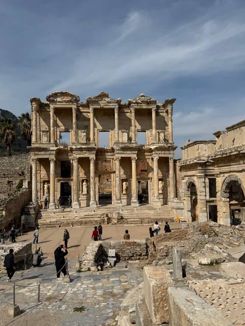       The grand façade of the Library of Celsus in Ephesus with visitors walking below its columns.
  