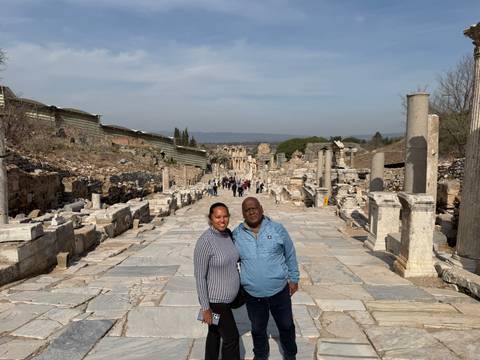       Smiling couple posing on the marble Curetes Street amid ruins of ancient Ephesus.
  