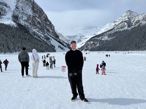       Frozen Lake Louise basin filled with visitors surrounded by dense snowy forests and towering peaks.
  